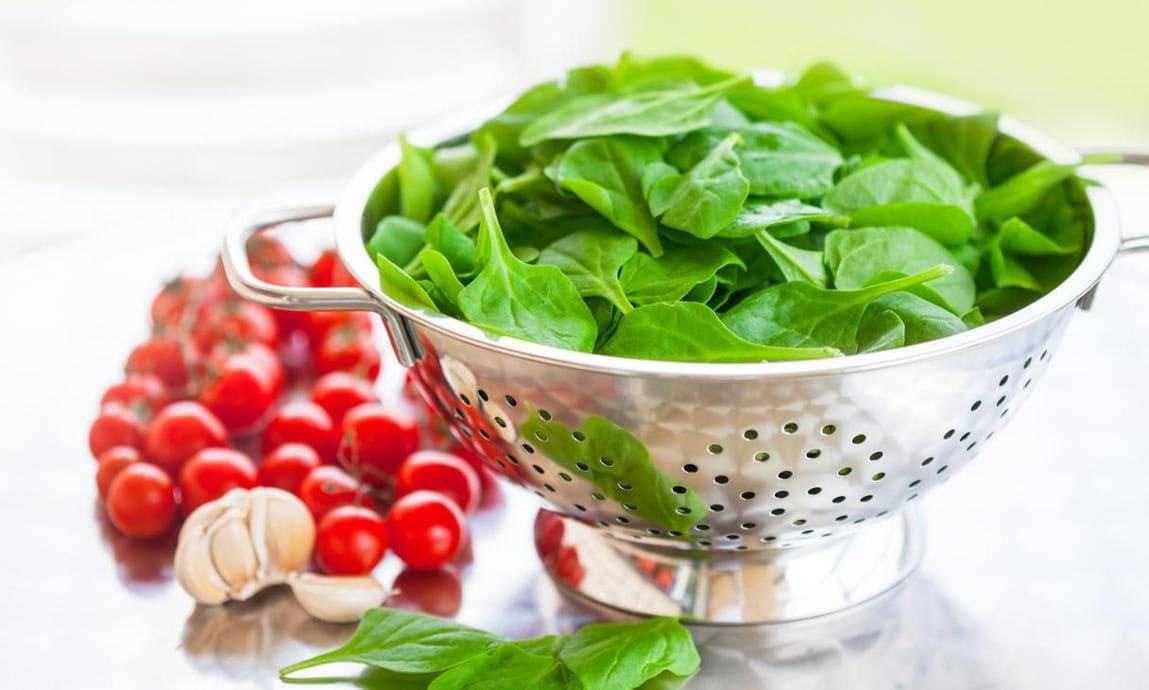 Garlic, cherry tomatoes, and colander with spinach leaves