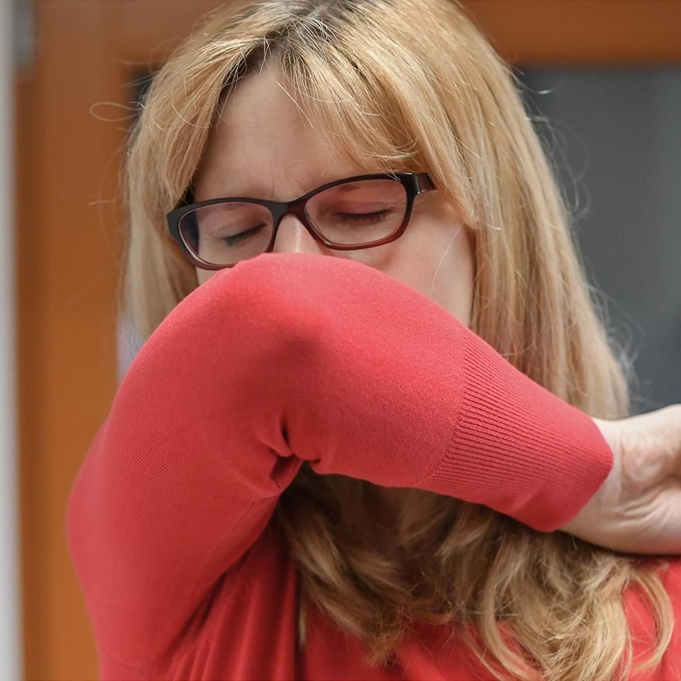 woman sneezing into elbow