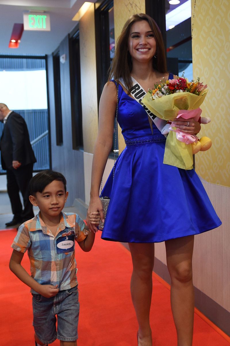 Miss Universe contestant Kseniya Alexandrova of Russia walks with a child from an orphanage during a visit to a popular fast food restaurant in Manila on December 7, 2017. 
