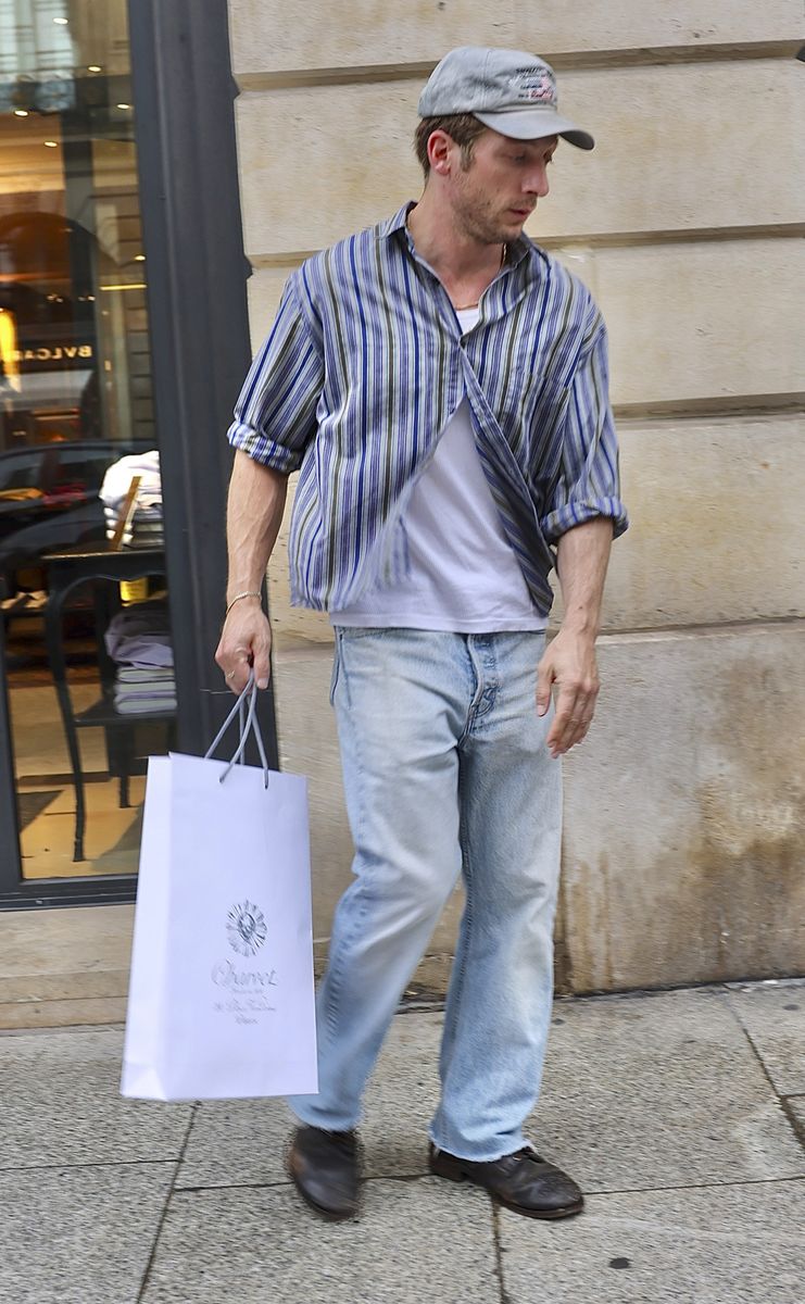 Jeremy Allen White keeps his Paris shopping look casual with a striped shirt, light-wash jeans and a gray baseball cap.