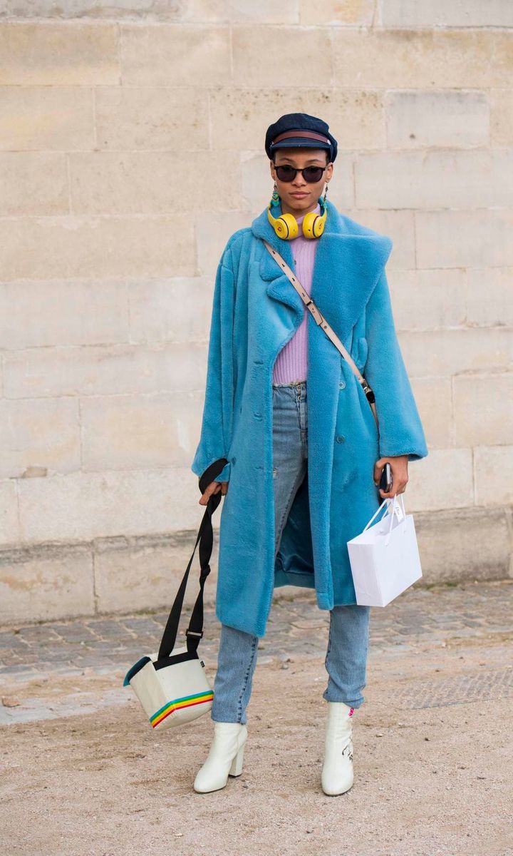 Model Lineisy Montero wears a Blue fake fur coat, purple jumper, blue jeans, navy flat cap and white boots