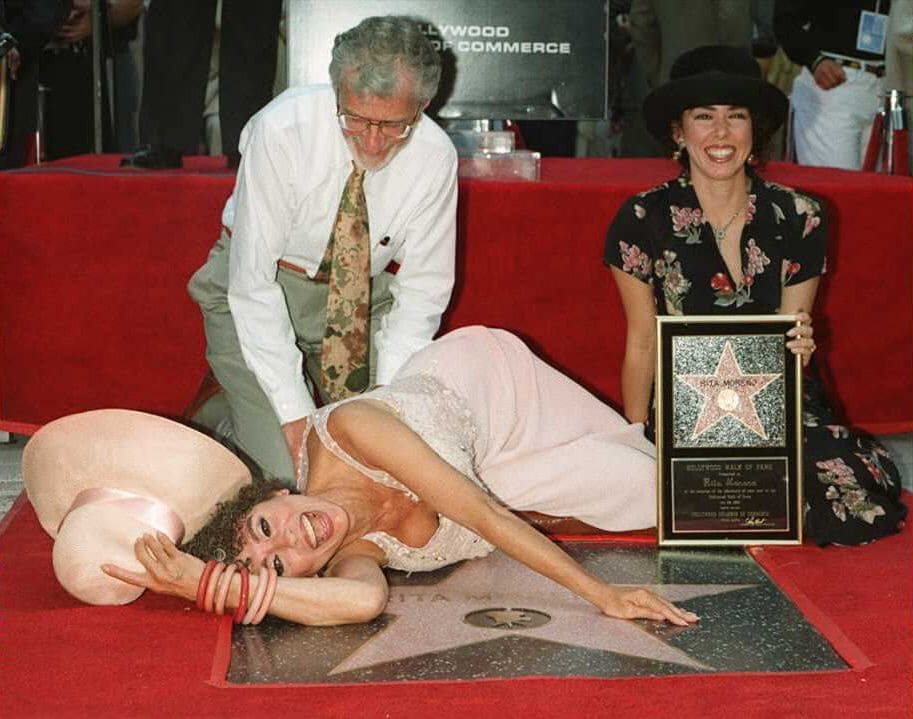 Rita Moreno lays down next to her star on the Hollywood Walk of Fame as her husband Leonard Gordan and daughter Fernanda Louisa watch