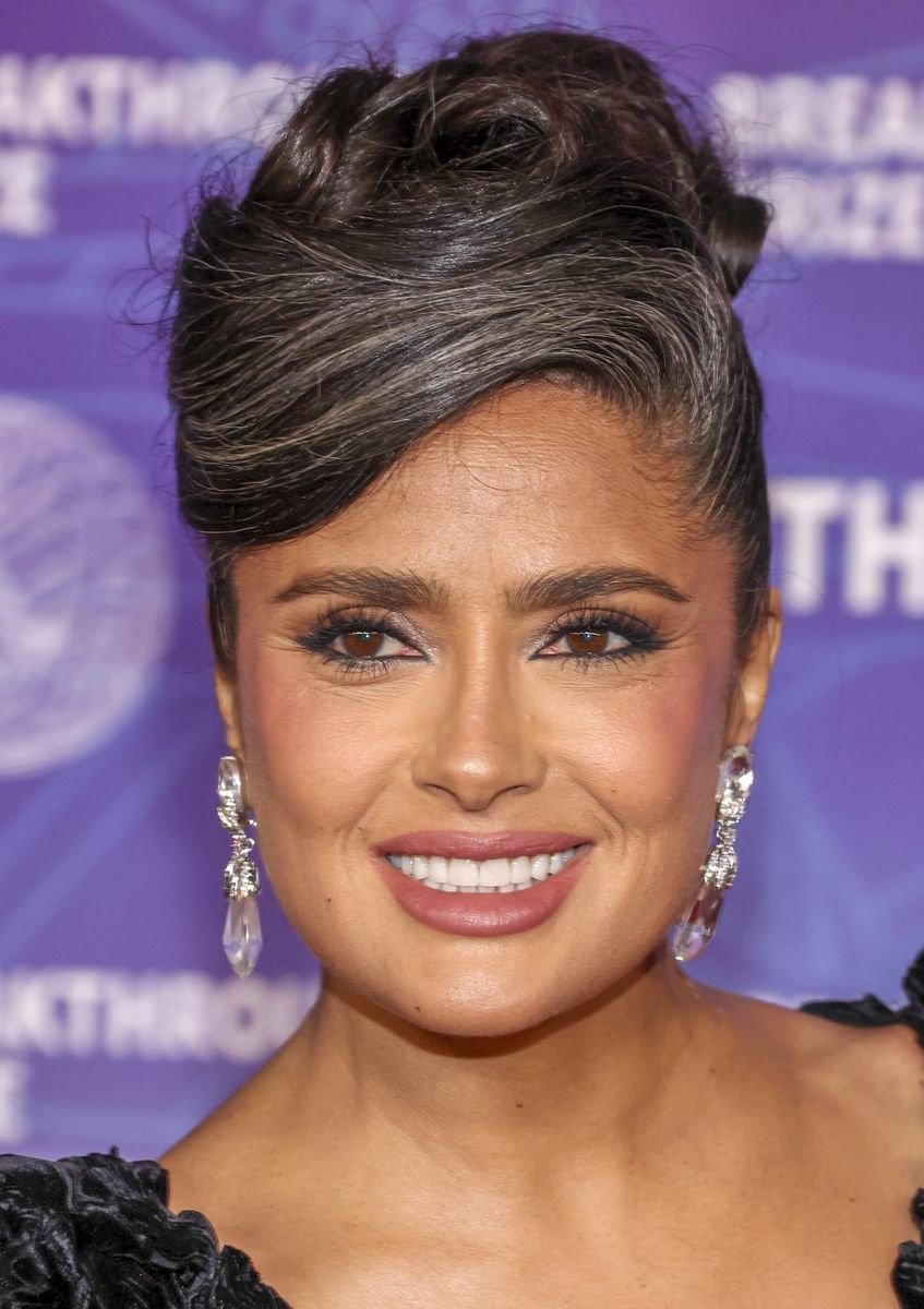 Salma Hayek debuts salt-and-pepper hair at the 2026 Breakthrough Prize, pairing a textured black gown with refined glam for a bold, modern red carpet statement.
