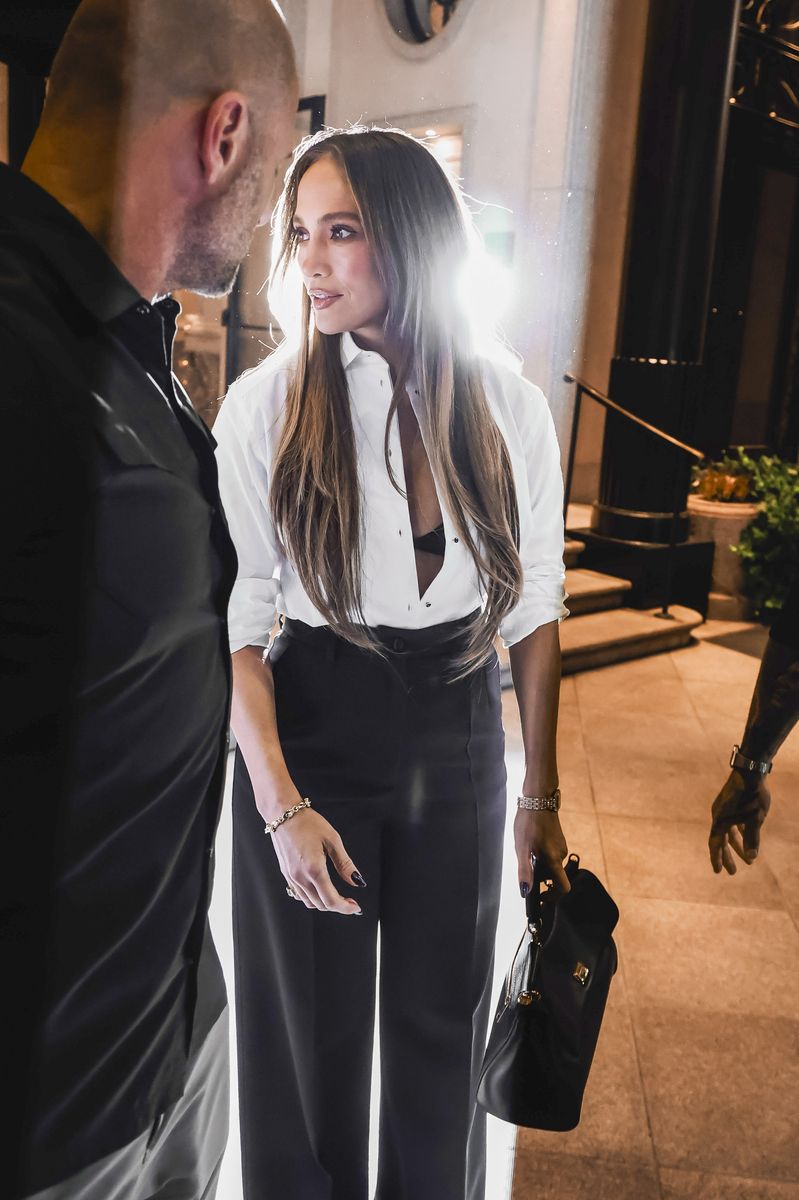 Jennifer Lopez is spotted during Milan Fashion Week wearing an open white shirt that reveals her bra, paired with high-waisted palazzo trousers and high platform heels.
