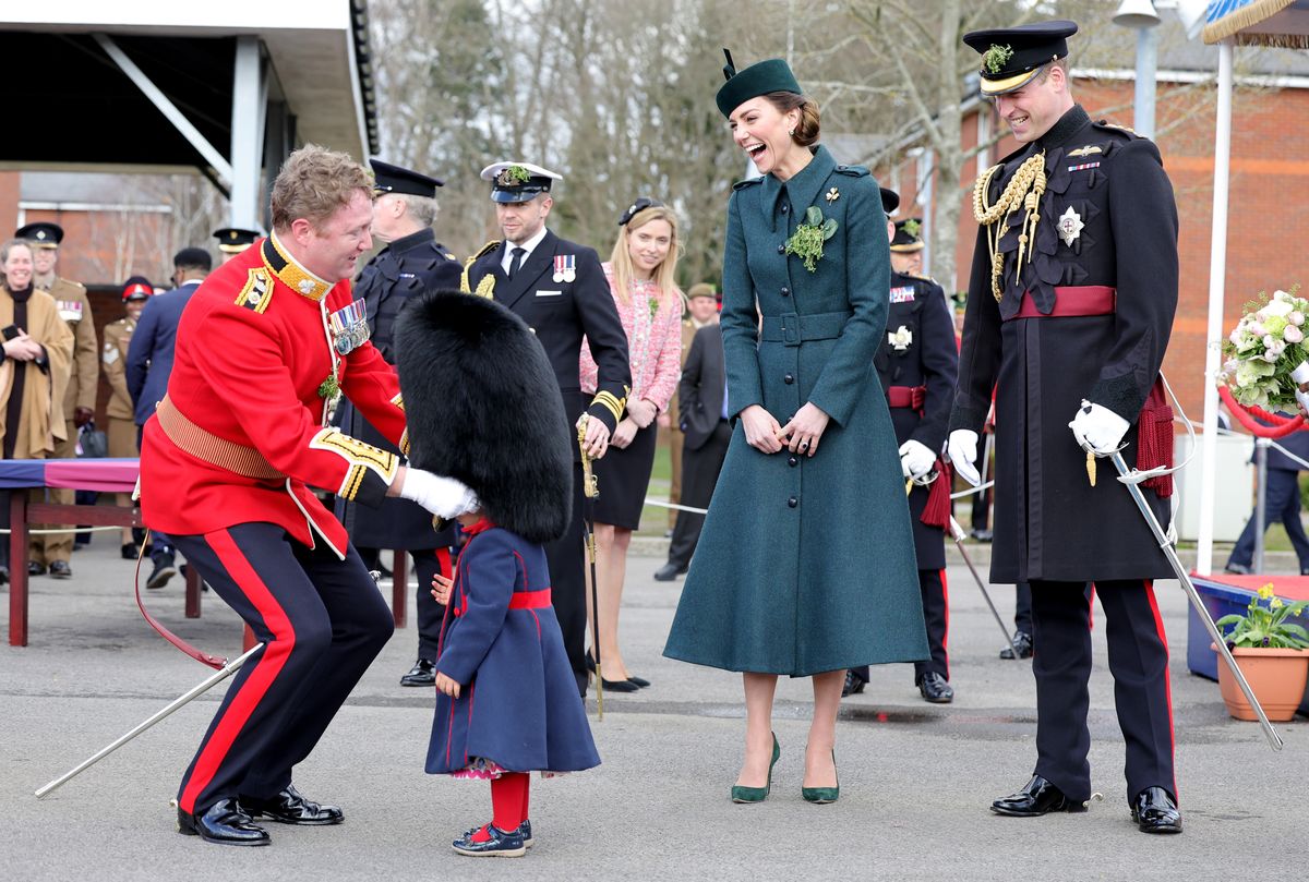 ALDERSHOT, ENGLAND - MARCH 17:  Catherine, Duchess of Cambridge and Prince William, Duke of Cambridge smile and laugh as Lieutenant Colonel Rob Money puts a bearskin hat on his 20-month-old daughter Gaia Money's head as they attend the 1st Battalion Irish Guards' St. Patrick's Day Parade at Mons Barracks on March 17, 2022 in Aldershot, England. (Photo by Chris Jackson - WPA Pool/Getty Images)