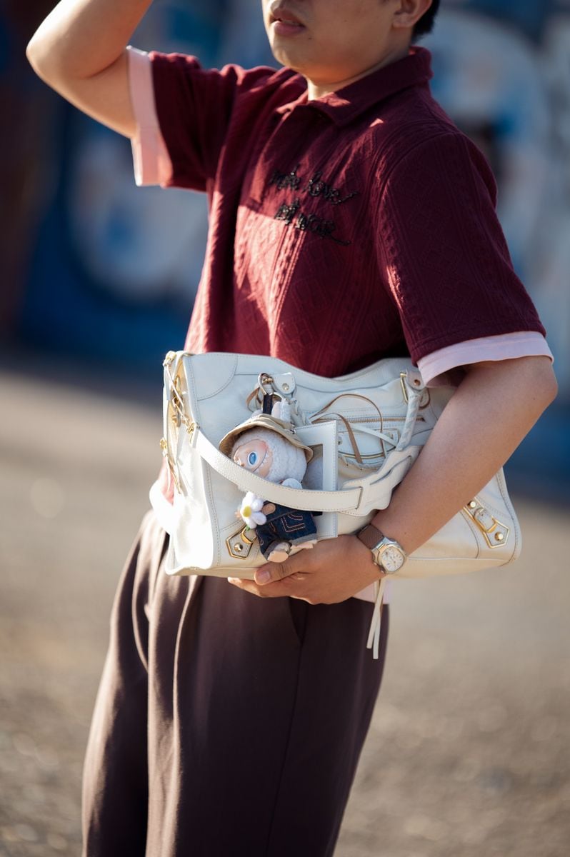 Gerald Hora wears brown pants, burgundy and pink shirt with words "make love not war" white bag with Labubu bag charm and mirrored sunglasses outside Rolf Ekroth during Copenhagen Fashion Week day two on August 05, 2025 in Copenhagen, Denmark. (Photo by Raimonda Kulikauskiene/Getty Images)