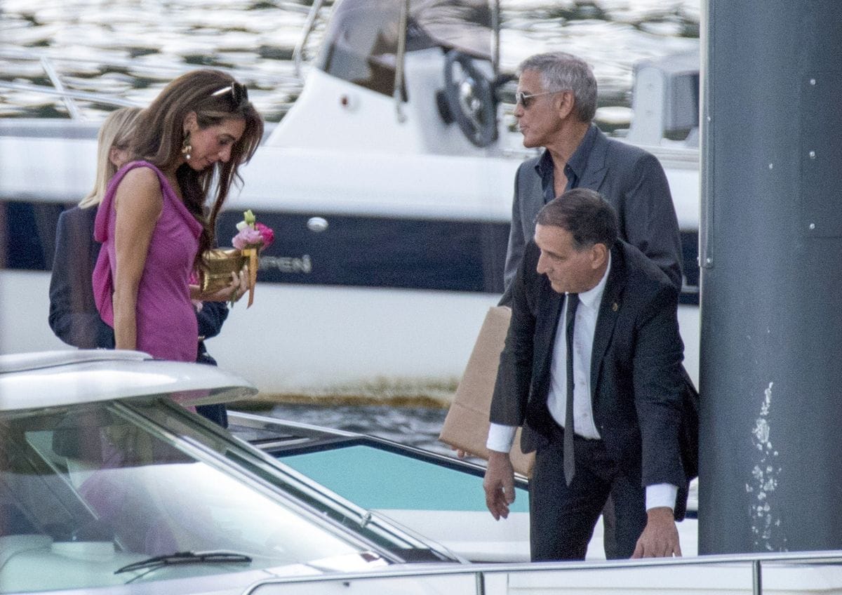 Amal wore a stunning fuchsia gown with a high slit and bow detail, paired with a gold clutch and pink bouquet, while George looked classic in a dark suit and open-collar shirt.