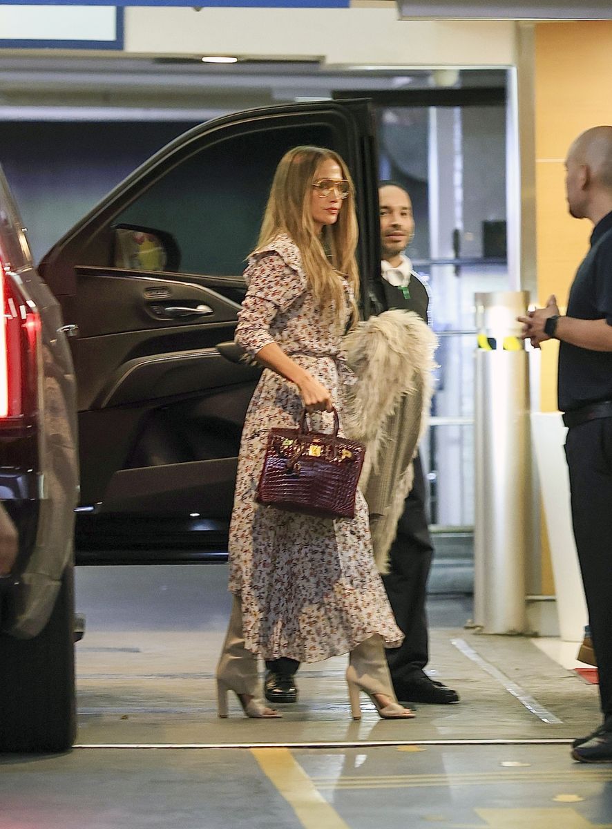 
Jennifer Lopez in a floral long dress, long open-toe boots, a fur vest, and a burgundy Birkin bag.