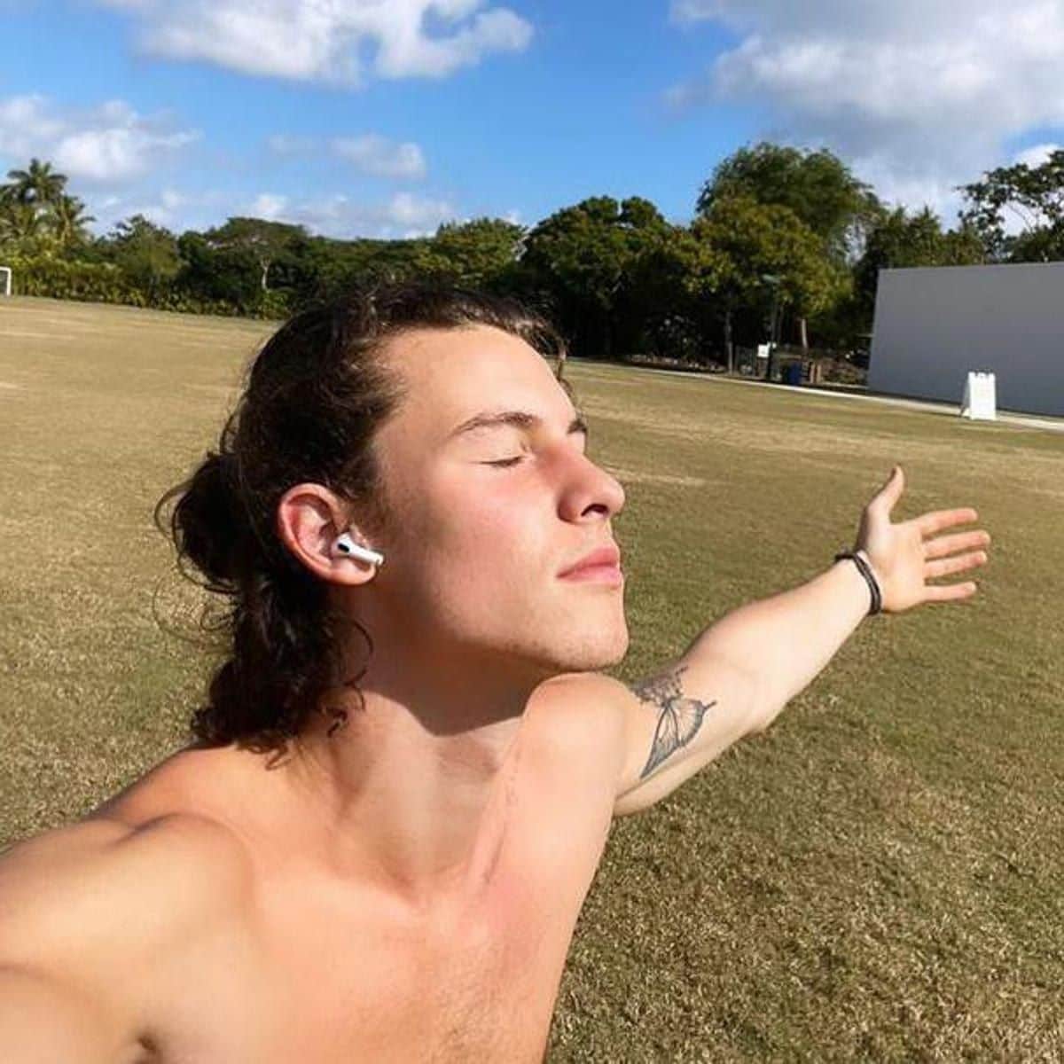 Shawn Mendes shirtless with his arms wide open outside.