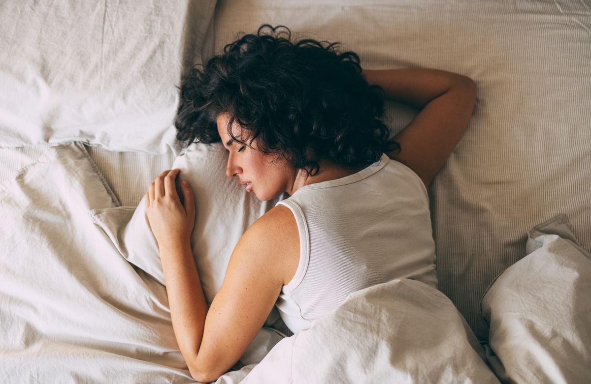 A woman with curly hair peacefully sleeping in a cozy bed, showcasing relaxation and restfulness. Perfect representation of comfort and tranquility for a restful night. 