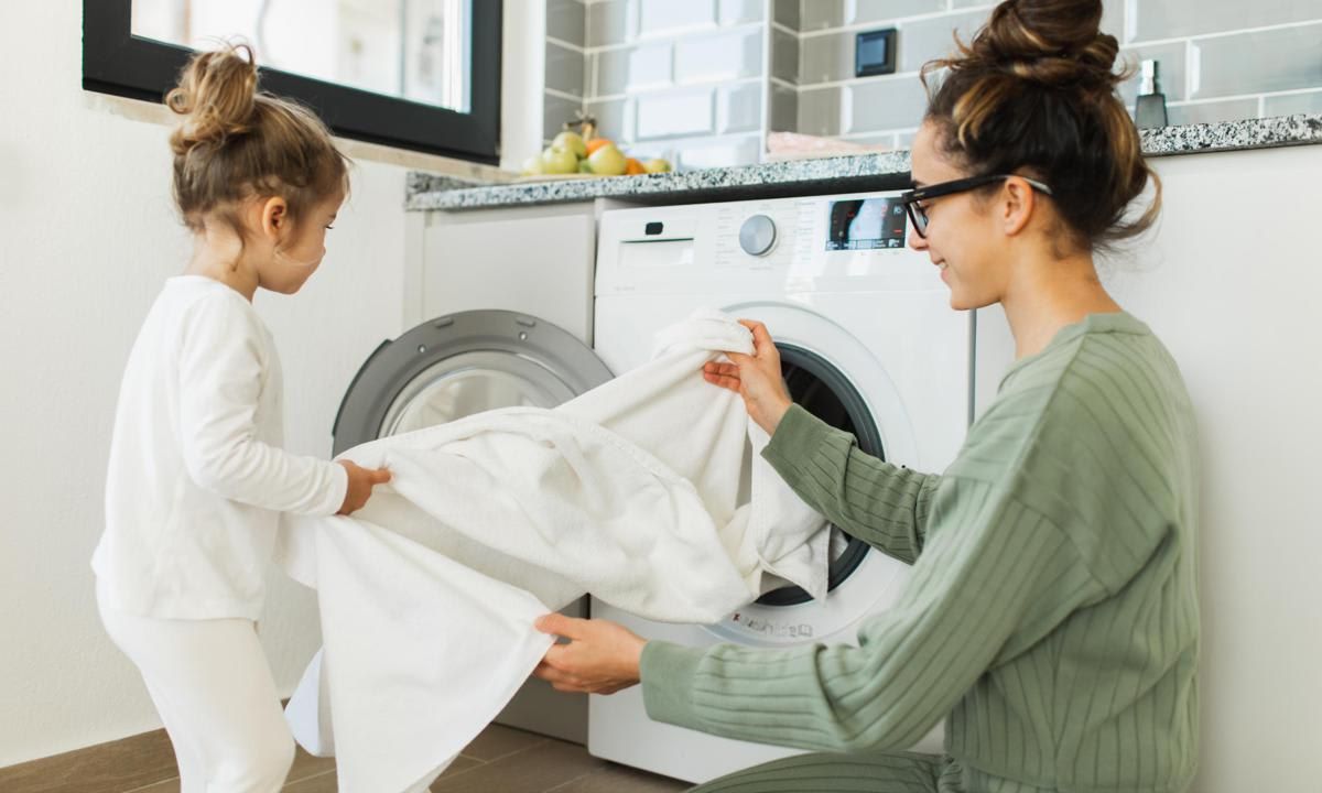 Mother and child girl little helper loading washing machine.