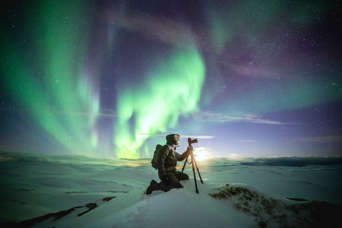 Photographer with tripod watching the green Aurora Borealis