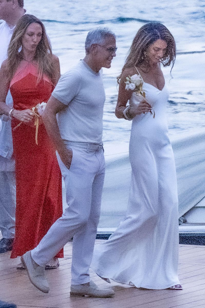 Amal Clooney looked radiant in a slinky white dress as she arrived by boat in Lake Como with George Clooney.