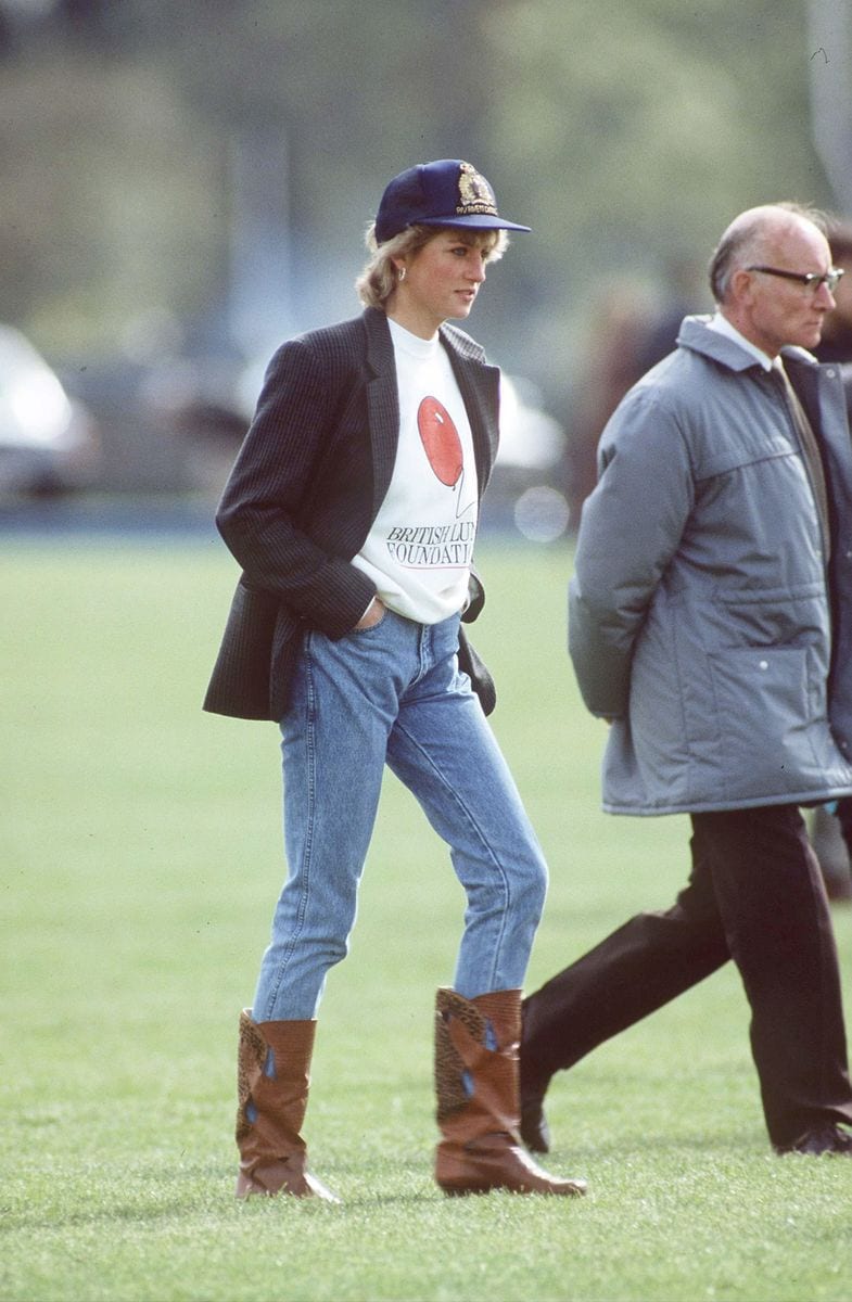 Princess Diana wearing a sweatshirt, baseball cap, boots and jeans.