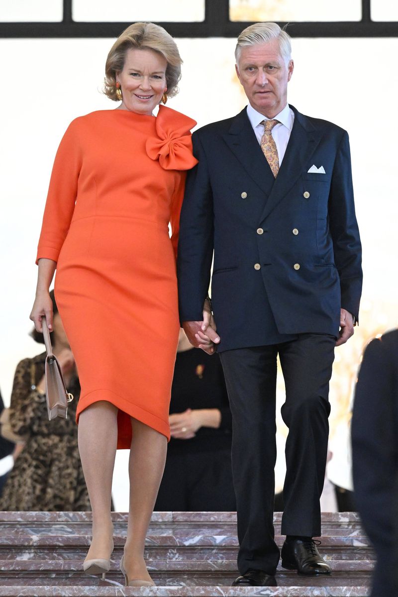 Queen Mathilde embraced bold color in an orange dress, with an oversized bow adding a playful touch to its classic silhouette.