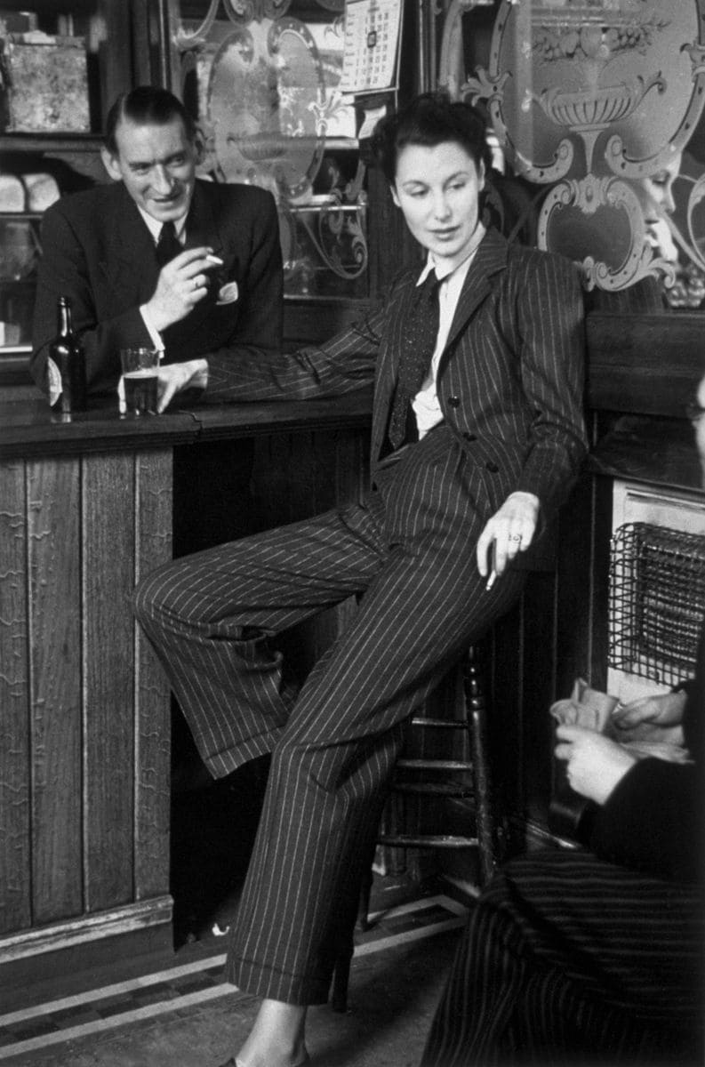 Journalist Anne Scott James, sitting at the bar in a pub, wearing a smart pinstripe suit and tie.  