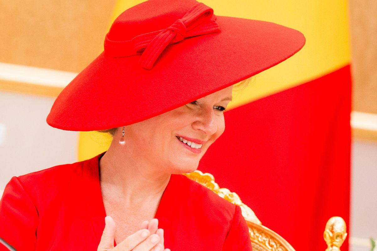 A matching bow decorates Queen Mathilde’s statement hat, while pearl drop earrings add an elegant finishing touch.