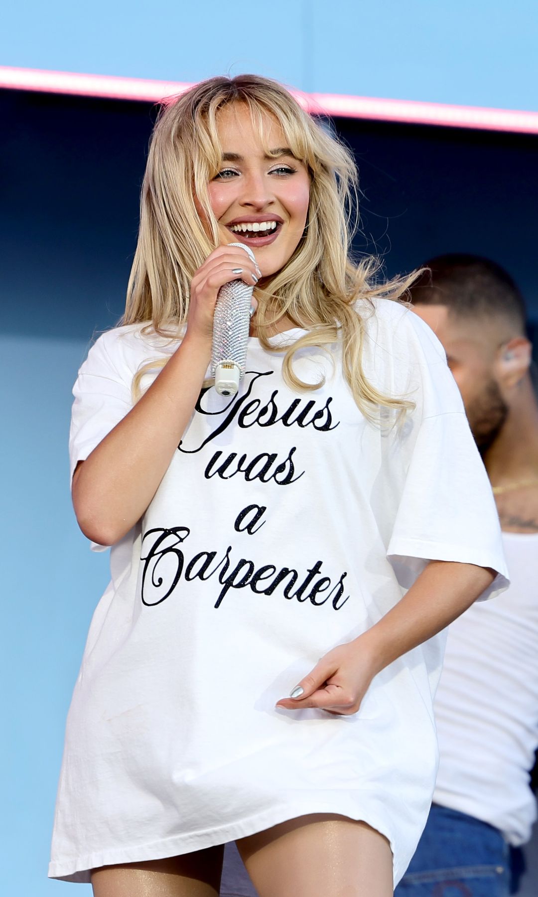 Sabrina Carpenter performs at the Coachella wearing an oversized white t-shirt. She completes her look with her classic loose, wavy hair.