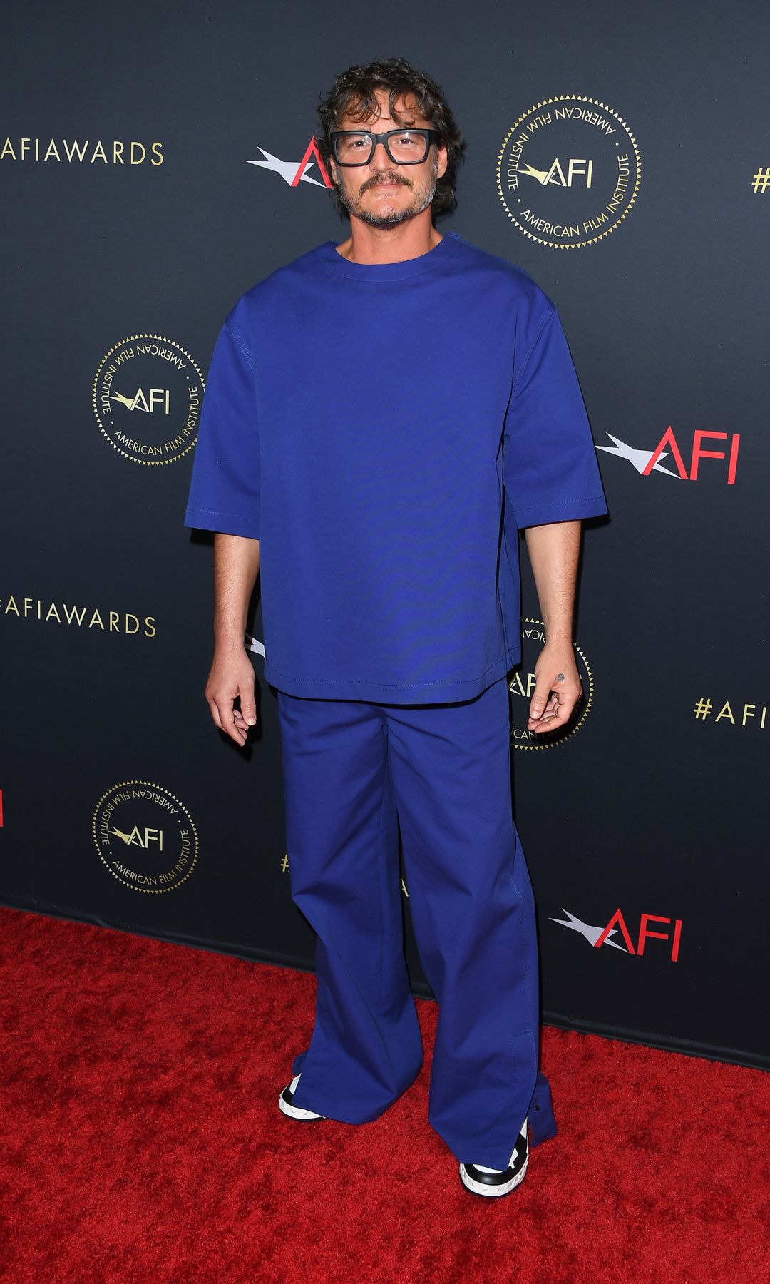 Pedro Pascal Wearing an oversized blue outfit combined with transparent glasses.