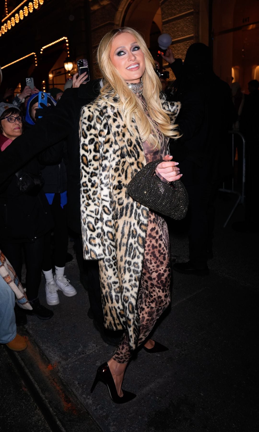 Paris Hilton in a full leopard-print look, featuring a long coat, stiletto heels, and a black Weitzman bag.