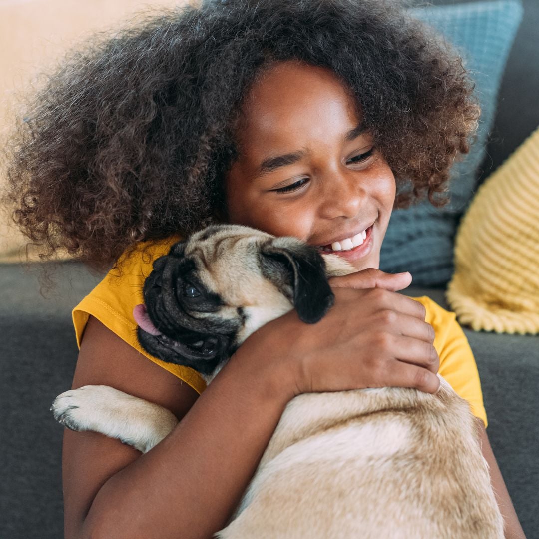 Shot of cute afro-american girl hugging her pug dog in the living room at home.