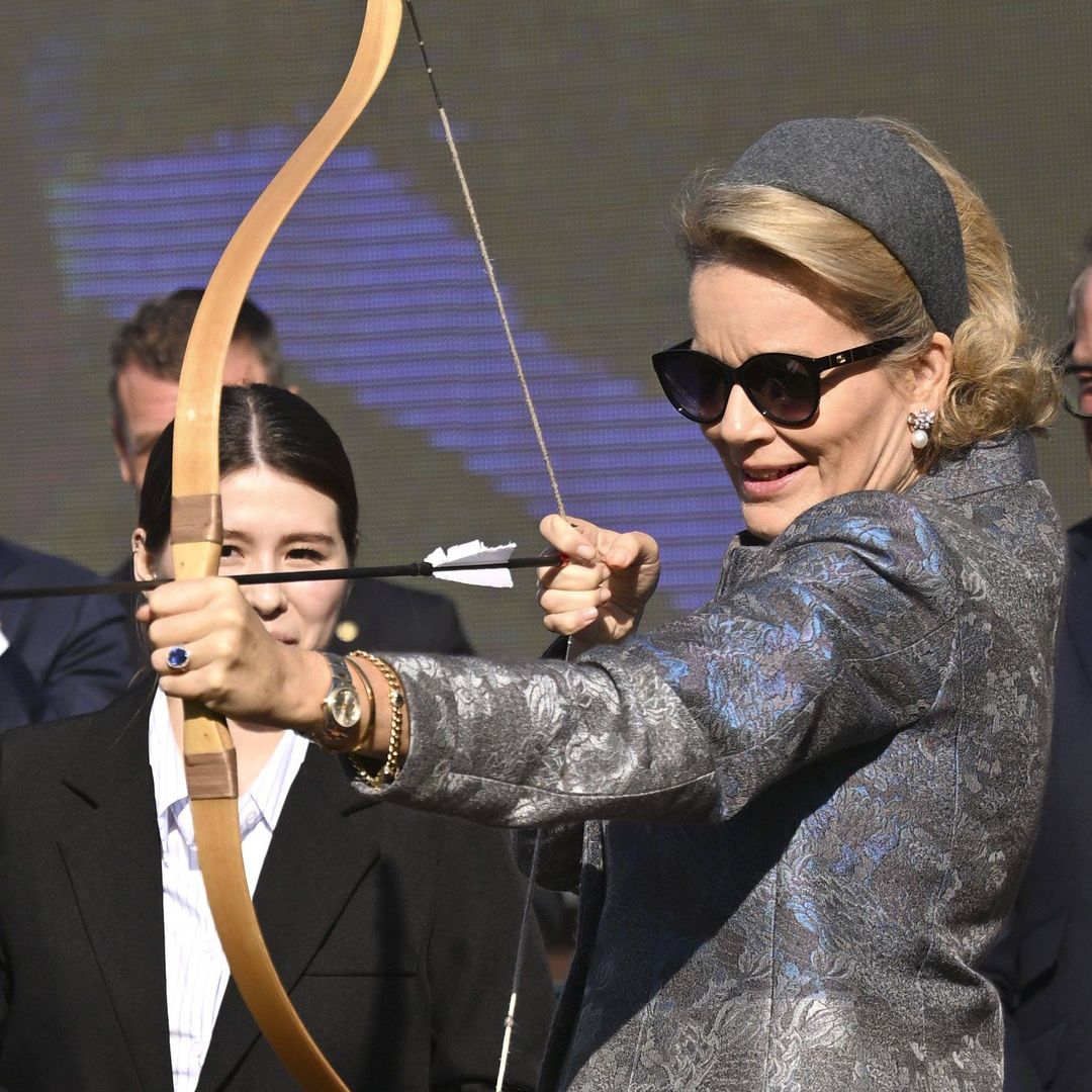 Queen Mathilde tries archery in heels and an elegant floral coat as King Philippe watches with a smile