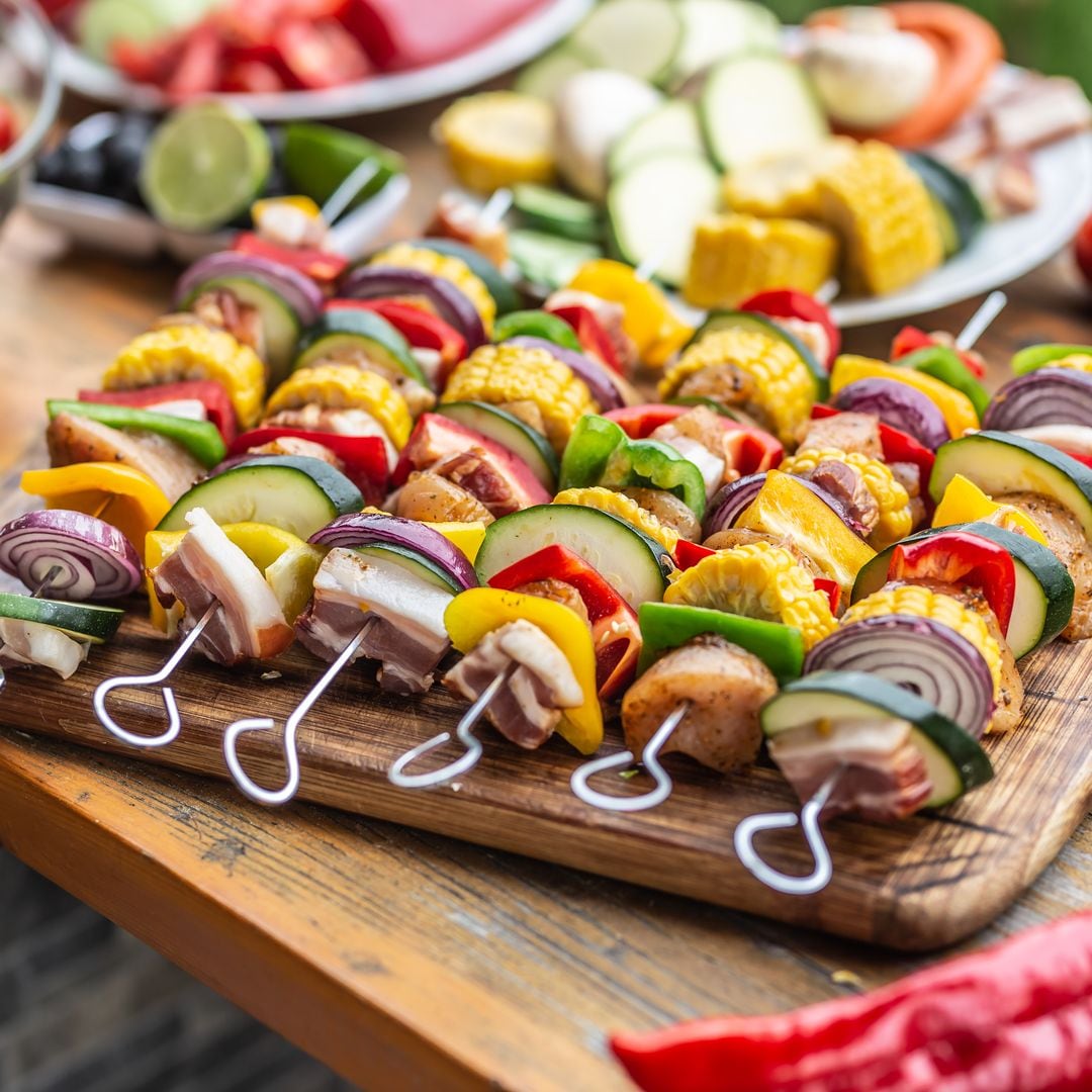Colorful meat and vegetable skewers ready for grill placed on awooden board outdoors on a garden table.