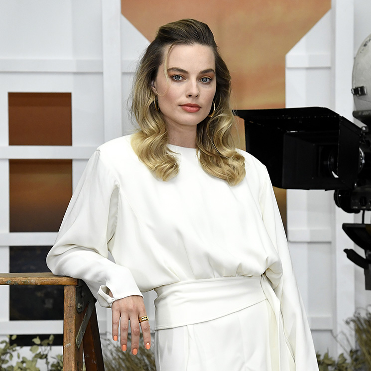 Margot Robbie con blusa marfil al lado de cámara de cine