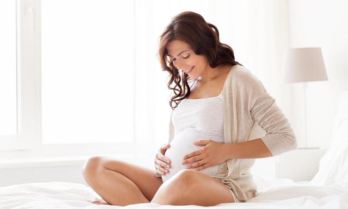 Mujer embarazada sentada en la cama y tocando su vientre en casa