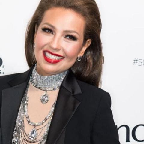 Thalía with her hair down, red lips, blouse with transparencies, and blazer.