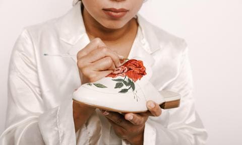woman painting red roses on white mules