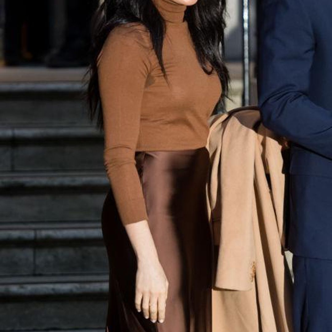 Meghan Markle con atuendo de falda satinada sueter y abrigo en colores tierra