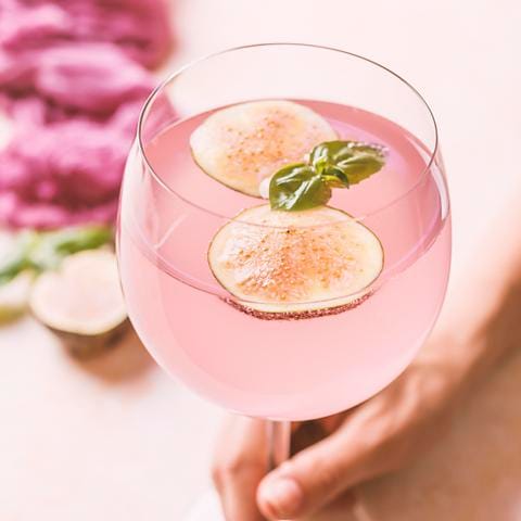Woman holding pink cocktail with fig and basil