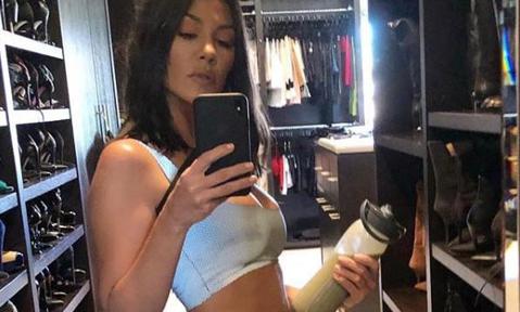 Kourtney Kardashian posing in the mirror in workout attire and holding a smoothie container