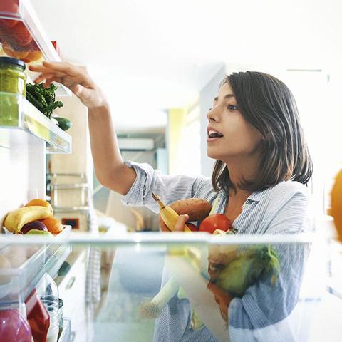 Young lady taking fruits and vegetables out of the fridge