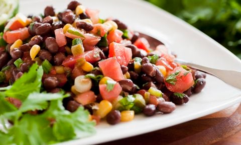 White plate with a serving of Black Bean Salad with cilantro garnish.