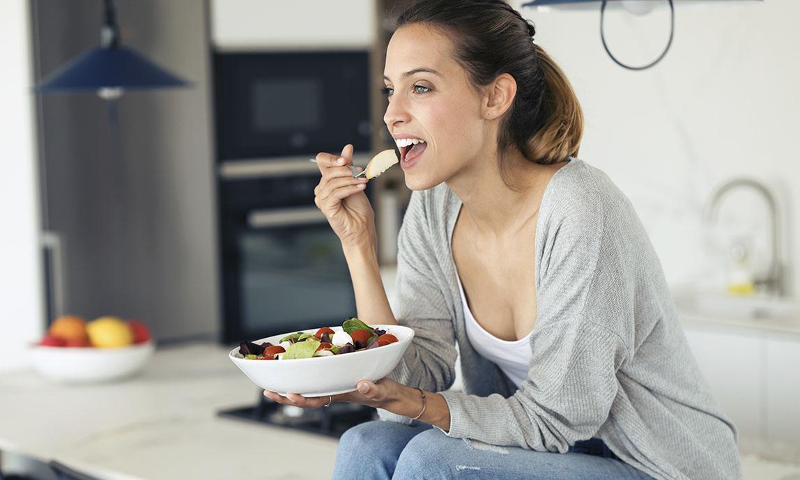 Mujer joven comiendo saludablemente en su cocina