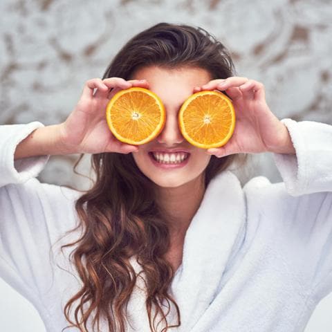 Mujer joven sostiene dos naranjas mientras sonríe y luce el cabello suelto