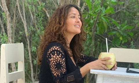 Salma Hayek wearing crochet dress and drinking coconut water.