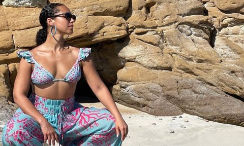 Alicia Keys poses on sand in blue and pink outfit.